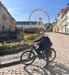 Eine Frau Ssteht mit einem Fahrrad vor einem Riesenrad, öffnet größere Ansicht