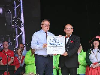 2 Männer stehen auf einer Bühne und halten ein Schild in die Höhe, öffnet größere Ansicht