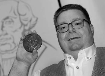 EIn Mann hält eine Medaille, öffnet größere Ansicht.