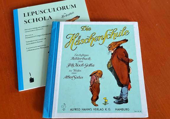 Eine lateinische Ausgabe von "Die Häschenschule" von Fritz Koch-Gotha und eine deutsche liegt auf einem Tisch.