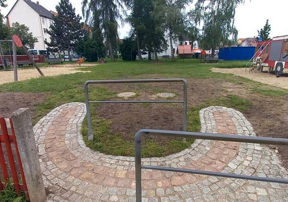 Eingang zum Spielplatz in der Gabelsbergerstraße Blick auf einen Spielplatz mit einem gepflasterten Smiley, im Hintergrund ist eine Schaukel und eine Spielzeugfeuerwehr zu sehen.