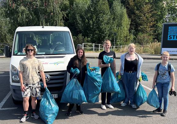 Alljährliche Müllsammelaktion des Kinder- und Jugendforums Kinder stehen mit blauen Mülltüten vor einem Kleinbus, öffnet größerer Ansicht.